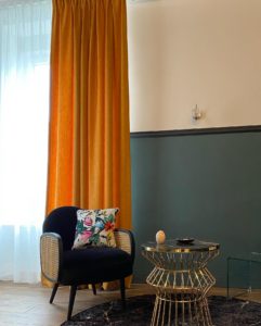 Visuel d'une vue sur un mur avec un fauteuil noir et un coussin imprimé florale avec un rideau derrière couleur orangé