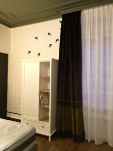 Photo de l'intérieur de la chambre avec une armoire ainsi que des rideau et une envolée d'hirondelles sur le mur blanc en arrière plan