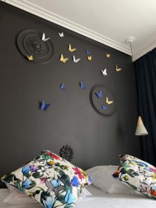 Mur noir avec des éléments graphique ne forme de cercle style cimaise avec une envolée e papillon au dessus de la tête de lit