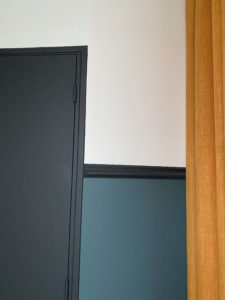 Photo d'une partie de la chambre avec une porte noire et une partie du rideau camelle